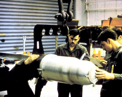 An image of three technicians working on the W80 'physics package', a slightly tapered metal cylinder 30cm wide and 80cm long - about as wide as a waste paper basket and about half as long as a person is tall.